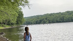 Un enfant se promène le long d’une rive rocheuse, avec une forêt en arrière-plan.