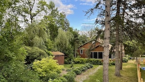 Une propriété résidentielle dotée d’un chemin en pierre, d’un abri en bois et d’une maison entourée d’une végétation luxuriante et d’arbres.