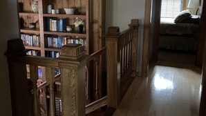 Un escalier en bois mène à une chambre à coucher qui contient un lit, une table de chevet et une fenêtre avec des stores.