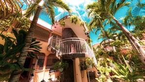A multi-level building with balconies, surrounded by lush tropical plants and palm trees.