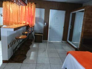 A hotel room with a kitchenette, a dining area with stools, a trash bin, and a sliding door. - Comfort Apartment STUDIO (10) RESIDENCE TROPICAL GARDEN (Boca Chica)
