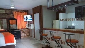 A hotel room with a bed, a TV, a kitchen area with a refrigerator, and a bar with stools.