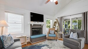 A living room with a fireplace, a television, a sofa, a chair, and a window with curtains. - Cute Family Beach Home in Wild Dunes Resort; Close to the Beach w/Porch Swing & Community Pool! (Isle Of Palms)