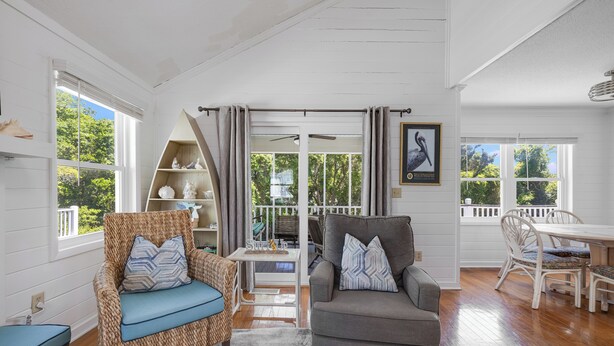 A spacious living area with a wicker chair, a gray sofa, and a dining table with white chairs. - Cute Family Beach Home in Wild Dunes Resort; Close to the Beach w/Porch Swing & Community Pool! (Isle Of Palms)