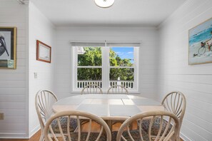 A dining area with a white table and chairs, a window with a view of trees, and a painting on the wall. - Cute Family Beach Home in Wild Dunes Resort; Close to the Beach w/Porch Swing & Community Pool! (Isle Of Palms)