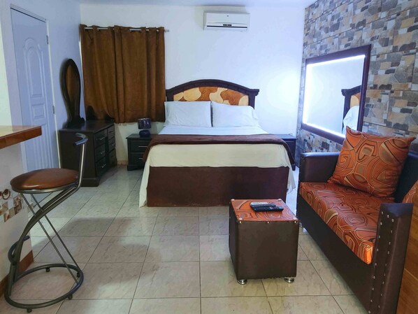 Un dormitorio con una cama, un sofá, una mesita, una silla, un escritorio y un espejo.