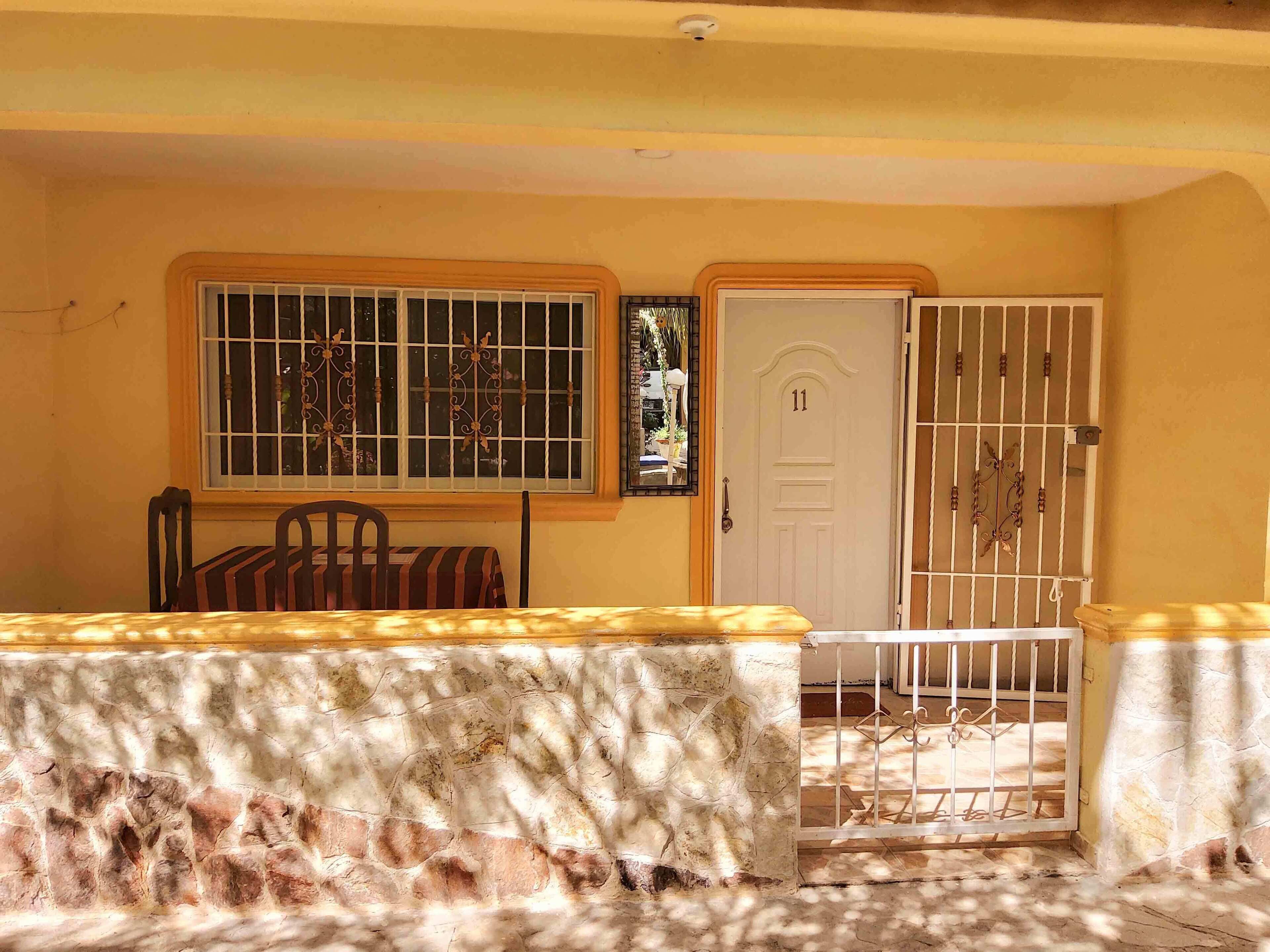Una habitación con una mesa, sillas, una puerta con barrotes y una ventana con rejas.