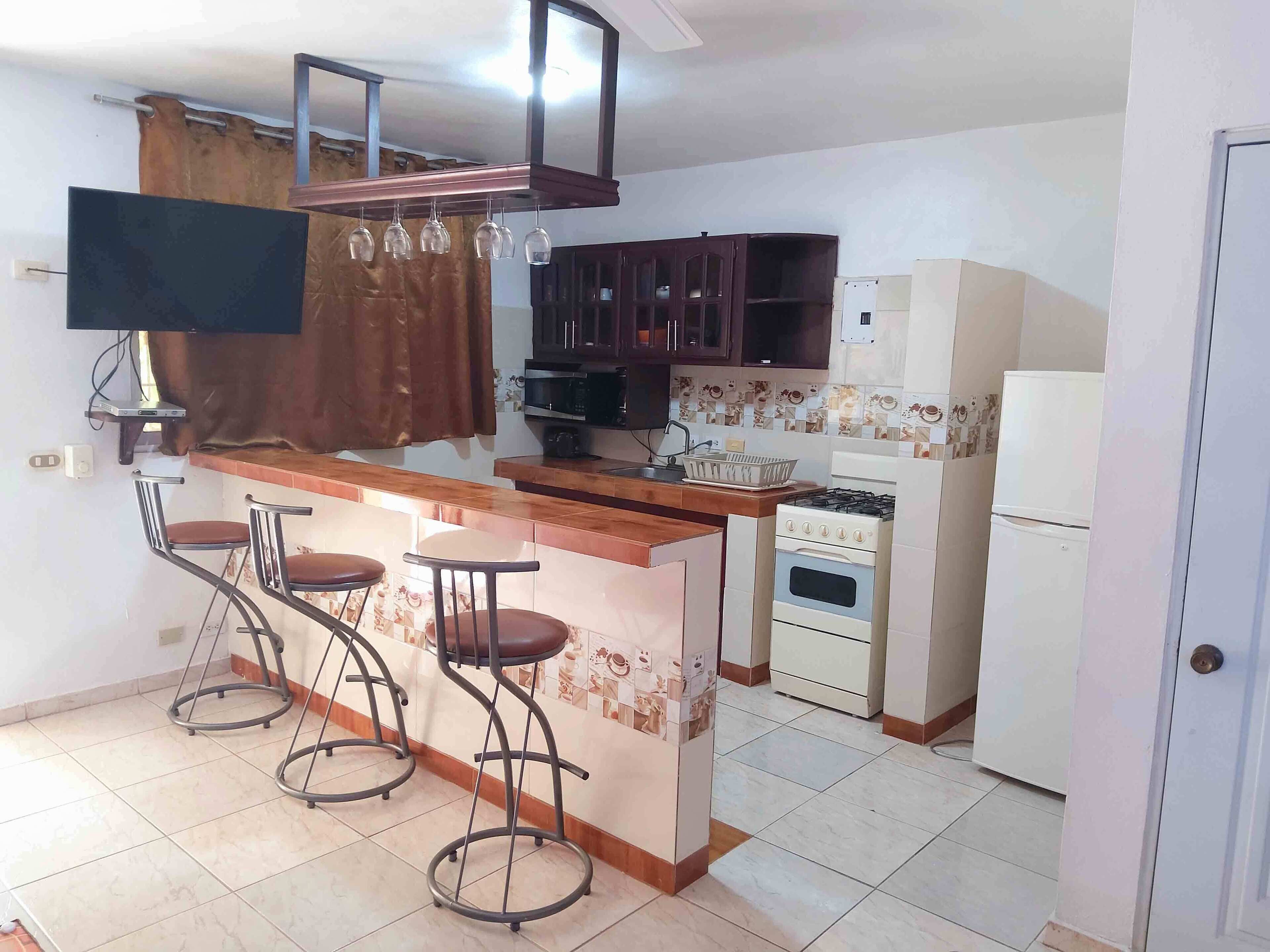 Una cocina con barra, estufa, microondas y refrigerador.