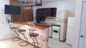 Una cocina con barra, estufa, microondas y refrigerador.