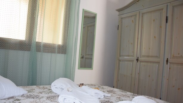 A neatly made bed with folded towels, a mirror, and a wardrobe in a hotel room. - The House in Sardinia Holiday Apartment (Olbia)