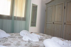 A neatly made bed with folded towels, a mirror, and a wardrobe in a hotel room. - The House in Sardinia Holiday Apartment (Olbia)