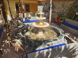 A stone fountain with water cascading down its tiers, surrounded by benches and potted plants.