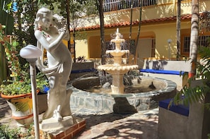 A tropical garden with a statue, a fountain, and a building in the background.