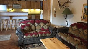 A cozy living room with a patterned sofa, a wooden coffee table, and a kitchen area in the background.