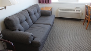 A grey sofa, a wooden side table, a chair, a radiator, and a window with curtains. - Downtown Jasper Suite Beautiful Views (Jasper)