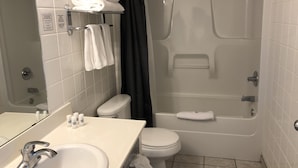 A bathroom with a sink, toilet, and bathtub. There are towels stacked on a shelf and a shower curtain. - Downtown Jasper Suite Beautiful Views (Jasper)