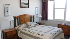 A neatly arranged bedroom with a bed, two bedside tables, a nightstand, a window with curtains, and two framed pictures on the wall. - Downtown Jasper Suite Beautiful Views (Jasper)