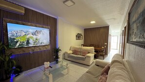 A modern living room with a flat-screen TV, a glass coffee table, a beige sofa, and a dining area with a wooden table and chairs. - Sea view holiday apartment (Torrevieja)