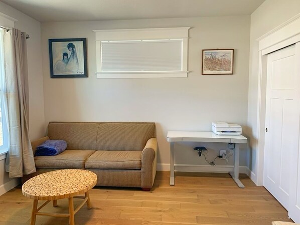 A living room with a beige sofa, a round wooden table, a white desk with a printer, and two framed pictures on the wall. - Amazing New Home in Bend...with hot tub! (Bend)