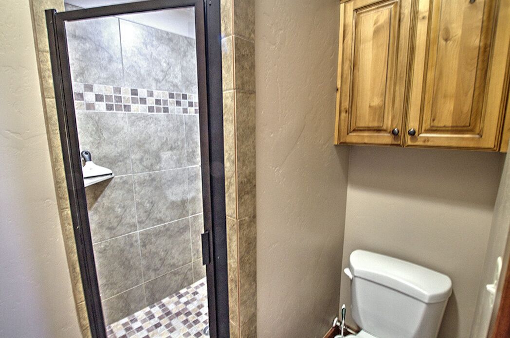 Een badkamer met een douchegedeelte, toilet en houten kastjes.