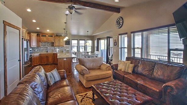 A spacious living area with leather sofas, a coffee table, and a fireplace. There is a kitchen in the background with wooden cabinets and a stone backsplash. - Private beach, pools/hot tub, winter sports, sleeps 20 (Fish Haven)