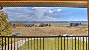 A view from a covered porch overlooking a large open field with a lake and mountains in the distance. - Private beach, pools/hot tub, winter sports, sleeps 20 (Fish Haven)