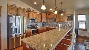A kitchen with granite countertops, stainless steel appliances, wooden cabinets, and pendant lighting. - Private beach, pools/hot tub, winter sports, sleeps 20 (Fish Haven)