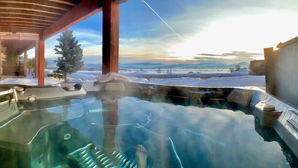 En utomhusbubbelpool med fri utsikt över ett snötäckt landskap och berg i bakgrunden.