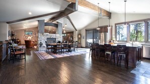 A spacious kitchen with high ceilings and exposed beams, a large dining area with multiple chairs, and a view of the outdoors through large windows.