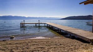 A wooden pier extending into calm water with clear skies and distant mountains.