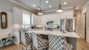 A modern kitchen with white cabinets, a large island with bar stools, stainless steel appliances, and pendant lighting. - Luxury 4BR Home! Walk to Beach & Bike to Pool! ~ The Wander Inn at WaterSound (Santa Rosa Beach)