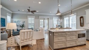 A spacious living room with a large white sofa, a coffee table, and a dining area with a kitchen island. - Luxury 4BR Home! Walk to Beach & Bike to Pool! ~ The Wander Inn at WaterSound (Santa Rosa Beach)