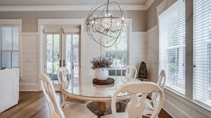 Un coin repas avec une table ronde, des chaises blanches, un lustre et une plante en pot.