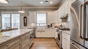 A modern kitchen with white cabinetry, stainless steel appliances, and a wooden floor. - Luxury 4BR Home! Walk to Beach & Bike to Pool! ~ The Wander Inn at WaterSound (Santa Rosa Beach)
