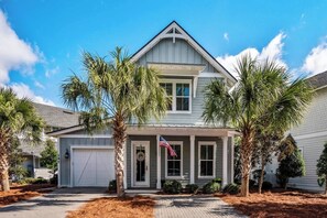 A two-story house with a front porch, a garage, and a flag. - Luxury 4BR Home! Walk to Beach & Bike to Pool! ~ The Wander Inn at WaterSound (Santa Rosa Beach)