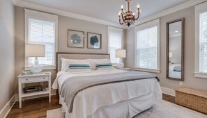 A bedroom with a large bed, two bedside tables, a chandelier, and a mirror.