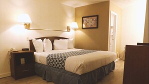 Un lit bien fait, recouvert d’une couvre-lit à motifs, deux lampes de chevet, une table de chevet avec un téléphone et un tableau encadré au mur.