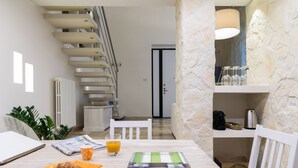 Une table de petit-déjeuner avec un croissant, un verre de jus d’orange et un magazine. On aperçoit un escalier au fond.