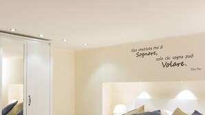 Une chambre moderne avec un lit blanc, de nombreux oreillers, une armoire et une citation affichée sur le mur.