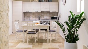 Une cuisine moderne avec des meubles blancs, une table à manger avec des chaises, une plante en pot et une horloge au mur.