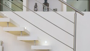 Un escalier moderne avec une rampe en métal et des marches blanches, menant à un palier où se trouve une console blanche et un objet décoratif.