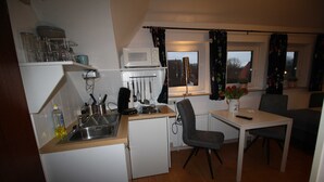A compact kitchen with a microwave, sink, and small refrigerator. There is a dining table with two chairs and a vase with flowers.