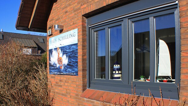 A brick building with a sign for 'Haus Schilling' and a window displaying a sailboat model.