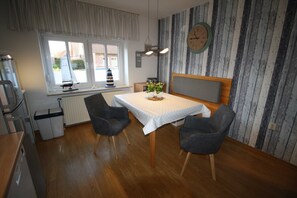 Et kompakt køkken med spiseplads, med et lille bord med to stole, et ur på væggen og et vindue med udsigt ud