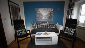Un saló amb una paret d'accent blau, un sofà estampat en blanc i negre, dues cadires negres, una taula de centre blanca i una fotografia en blanc i negre emmarcada.