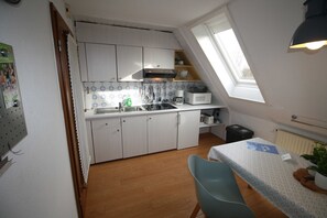 Pieni, käytännöllinen keittiö, jossa on valkoiset kaapit, mikroaaltouuni ja ikkuna.