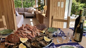 A dining table with seafood, a bottle of wine, and a view of a garden. - wood-panelled sailor's cottage a stone's throw from the port (Bénodet)