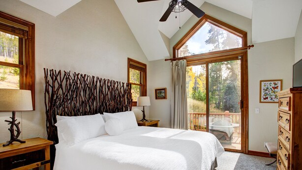 Een slaapkamer met een groot bed, een houten hoofdeinde, twee nachtkastjes met lampen, een dressoir en een balkon met uitzicht op bomen.
