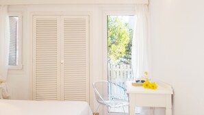 Ein Zimmer mit einem Bett, einem Schreibtisch mit Blumen und Blick auf Bäume durch ein Fenster.