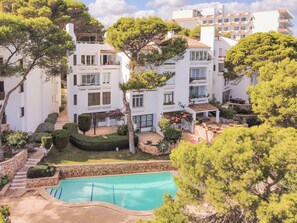 A residential complex with multiple white buildings, a swimming pool, and surrounding greenery.